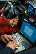Man sitting in a car using a diagnostic laptop